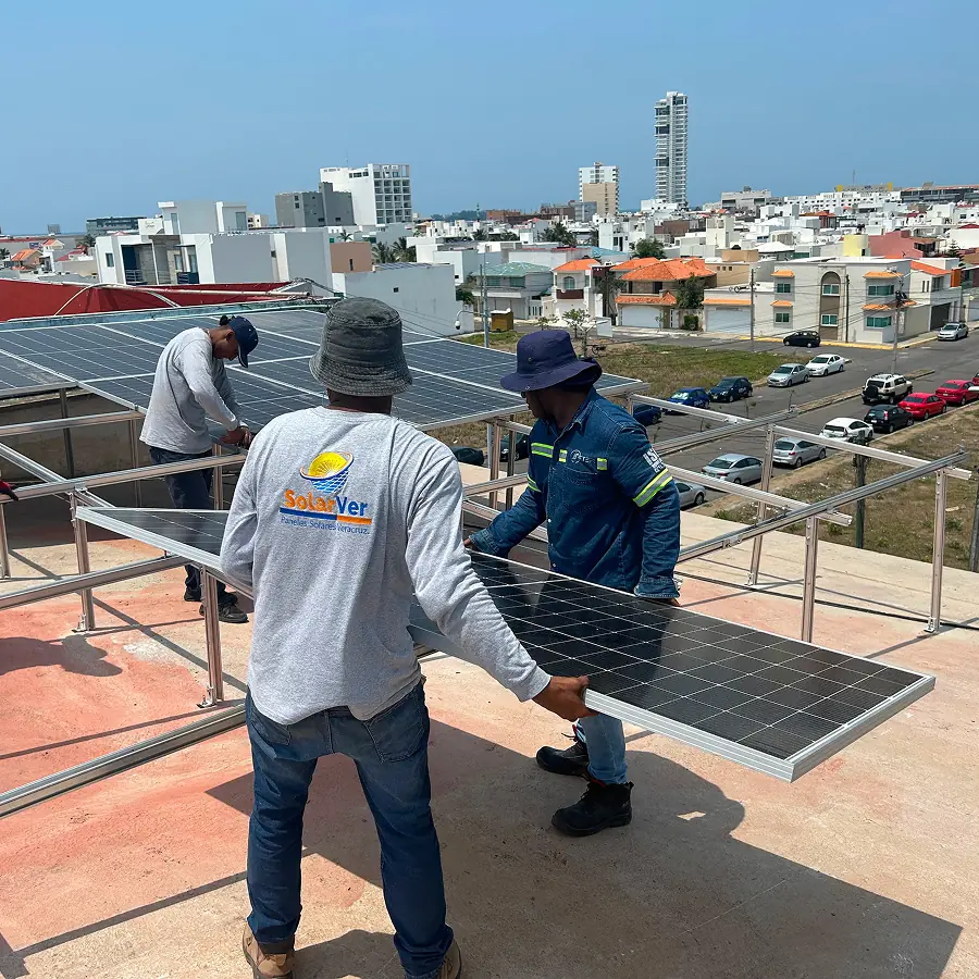 Cuadrilla de Solarver cargando un panel solar hacia su estructura en una azotea, con la ciudad al fondo.