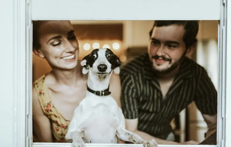 Una pareja sonríe con un perrito entre los dos.