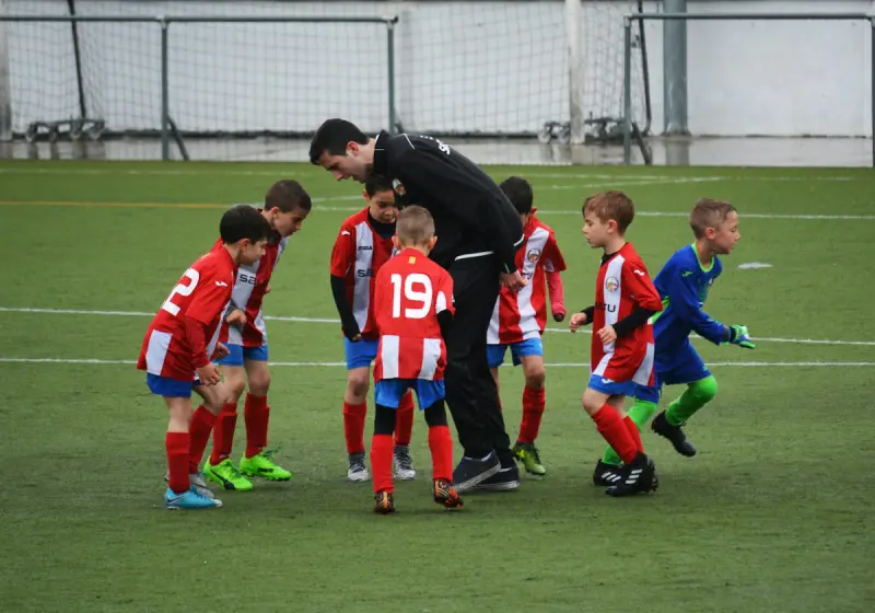 Niños con uniforme de fútbol escuchan a su entrenador en la cancha.