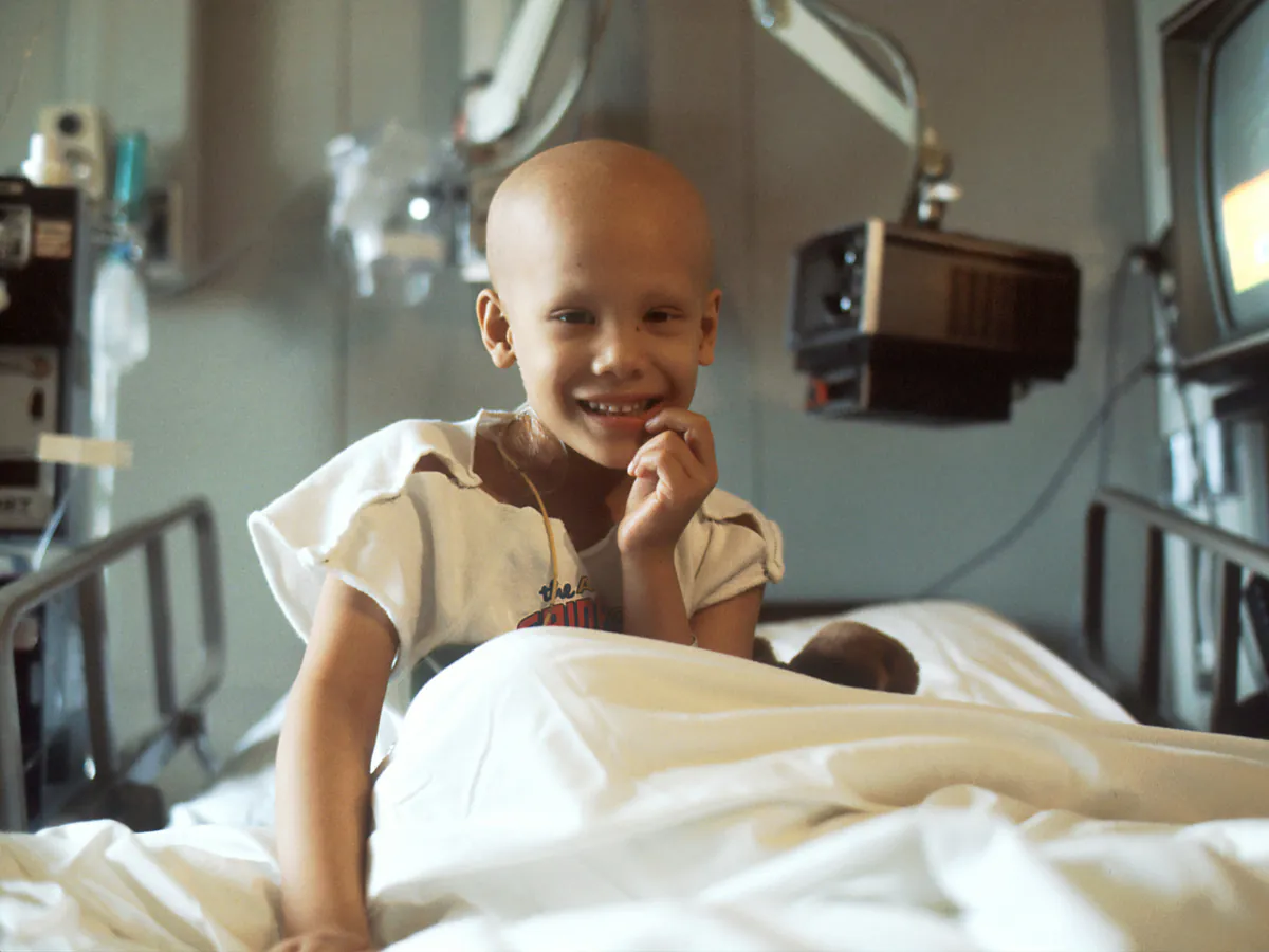 Un niño sin cabello sonríe desde su cama de hospital.