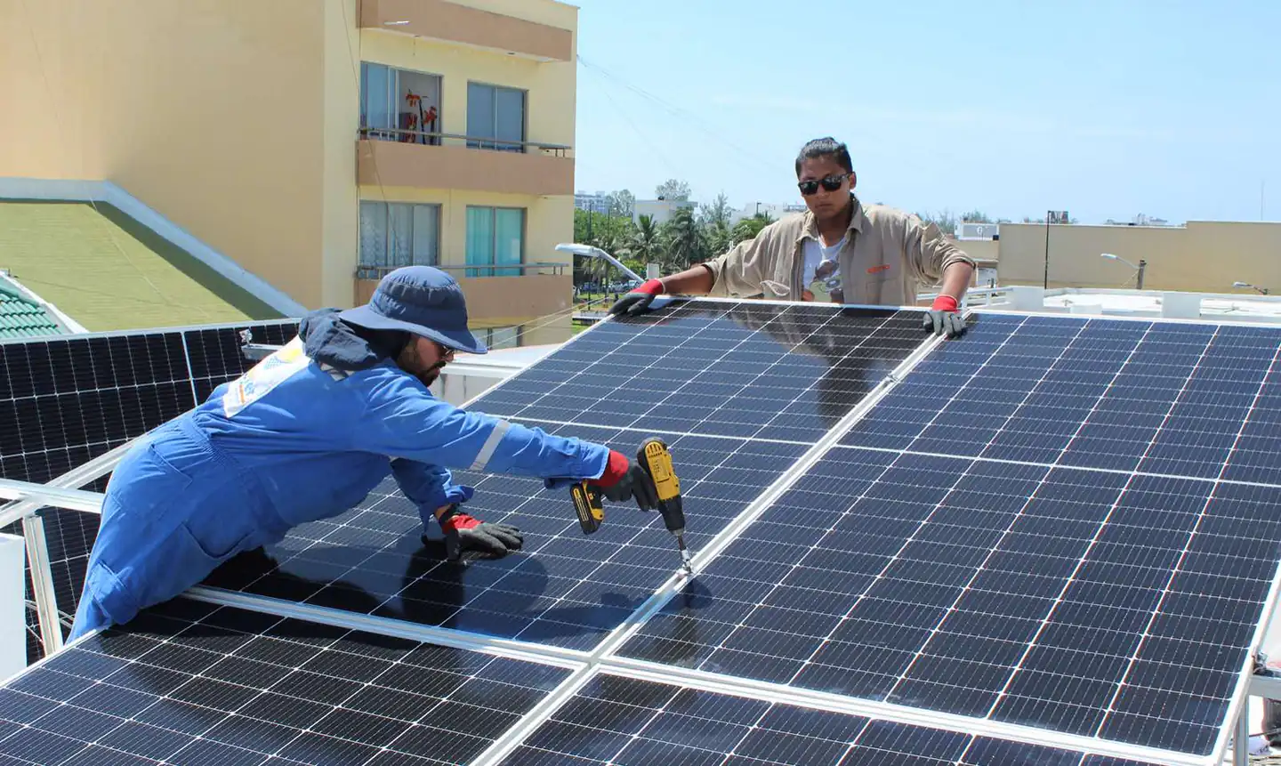 Dos instaladores de Solarver atornillando paneles solares sobre una azotea residencial, con la ciudad al fondo.